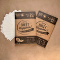 Load image into Gallery viewer, Two packages of 'Sheet Happens!' laundry detergent on a brown background