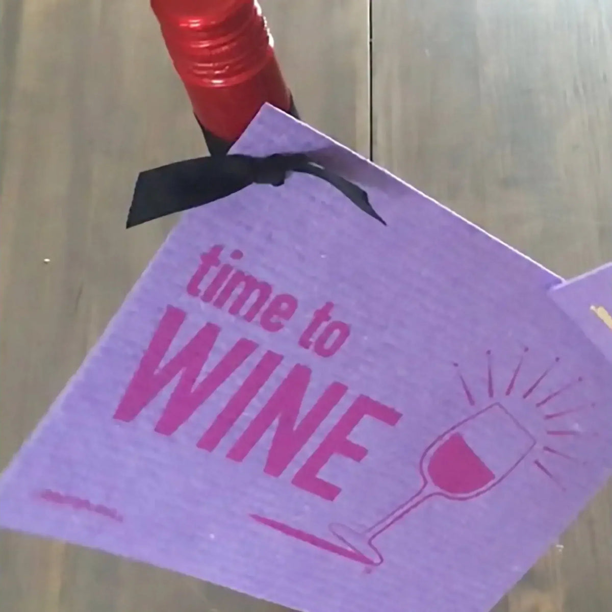 Purple time to wine bottle tag with pink lettering and glass tied on red-wrapped bottle for swedish dishcloth gift ideas