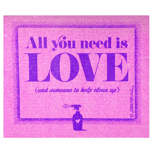 A Swedish dishcloth with graphic print in a pink and purple color scheme, featuring the text 'All you need is LOVE (and someone to help clean up)' in stylized lettering, with a small illustration of a spray bottle at the bottom.