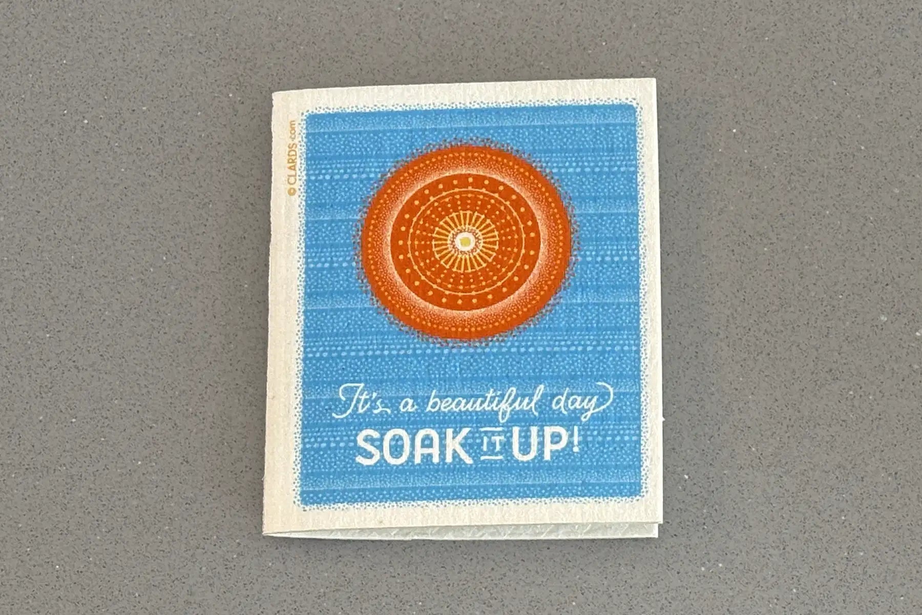 Blue and orange mandala-patterned sponge with ’it’s a beautiful day soak it up!’ printed on it.