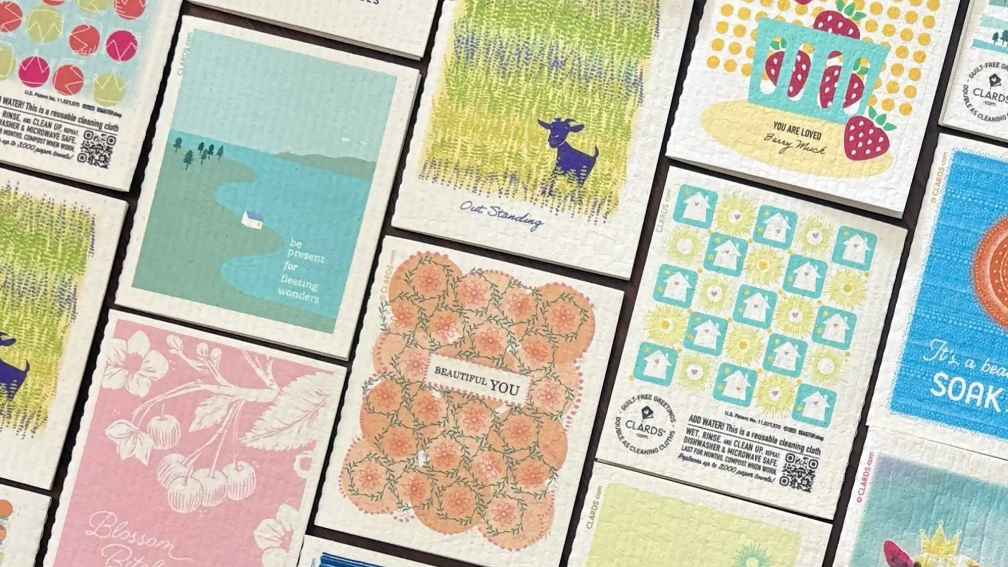 A collection of colorful, illustrated greeting Clards that turn into cleaning cloths featuring whimsical designs like goats in grass and strawberries.