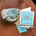 Load image into Gallery viewer, Greeting Clards on wood table showing greeting, pen and envelope and bowl of water with Clards turned into a cleaning cloth. It's Your Day Soak iT Up. soakitup.shop
